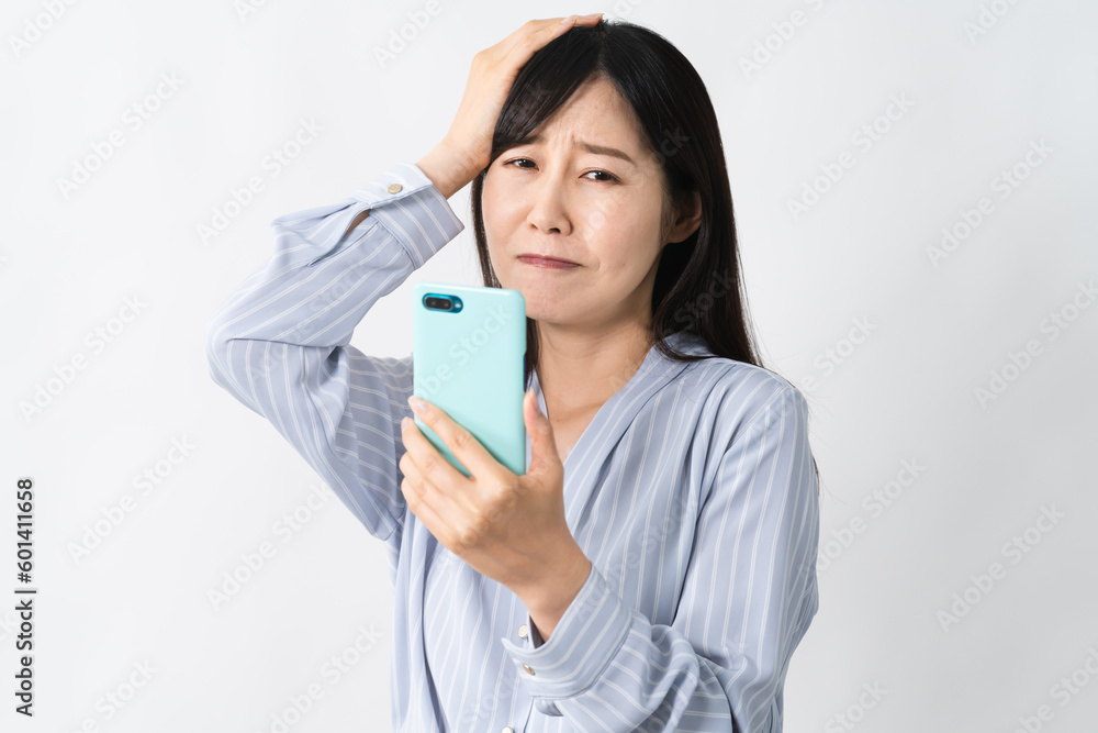 スマートフォンを持ちながら頭を抱える若い女性 スマートフォンを持ちながら頭を抱える若い女性