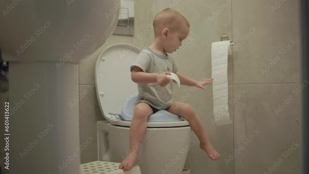 baby toddler sitting on toilet learning to clean his hygiene bottom butt anus toilet paper. potty training child in bathroom. little boy kid pulls toilet paper sweep his back after poop poo defecate baby toddler sitting on toilet learning to clean his hygiene bottom butt anus toilet paper. potty training child in bathroom. little boy kid pulls toilet paper sweep his back after poop poo defecate