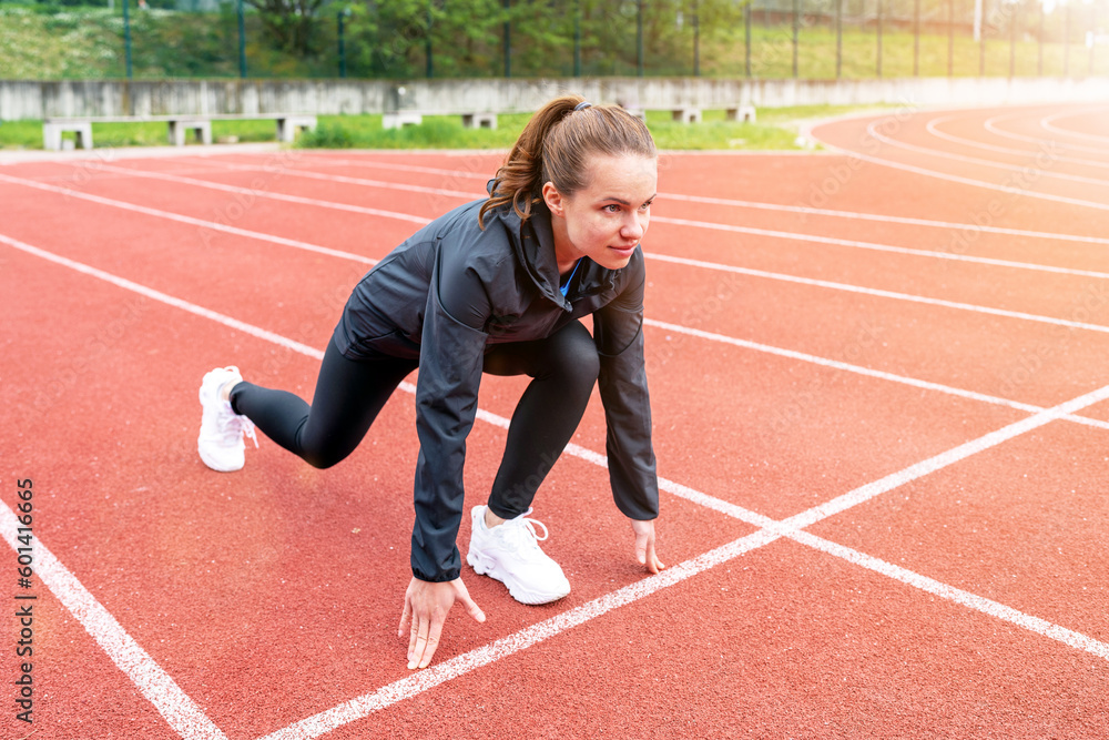 Brunette woman runner in start position on running track while workout. Brunette woman runner in start position on running track while workout.