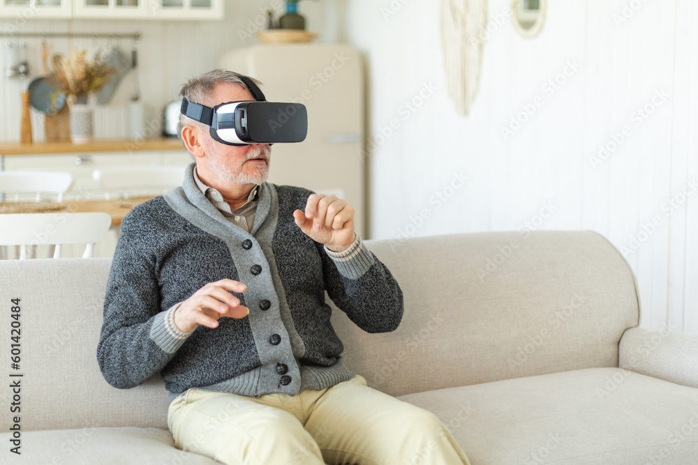Excited mature senior man wearing using virtual reality metaverse VR glasses headset at home. Grandfather touching air during VR experience on virtual reality helmet. Simulation hi-tech videogame Excited mature senior man wearing using virtual reality metaverse VR glasses headset at home. Grandfather touching air during VR experience on virtual reality helmet. Simulation hi-tech videogame