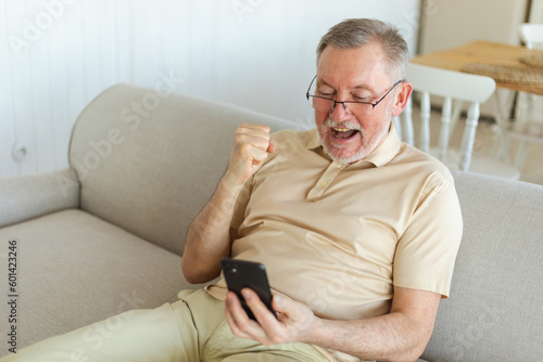 Middle aged senior man euphoric winner with smartphone. Older mature grandfather looking at cell phone reading great news getting good result winning online bid feeling amazed. Winning gesture