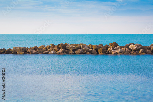 A quiet bay with crystal see water, rocks, sand and breakwater barrier