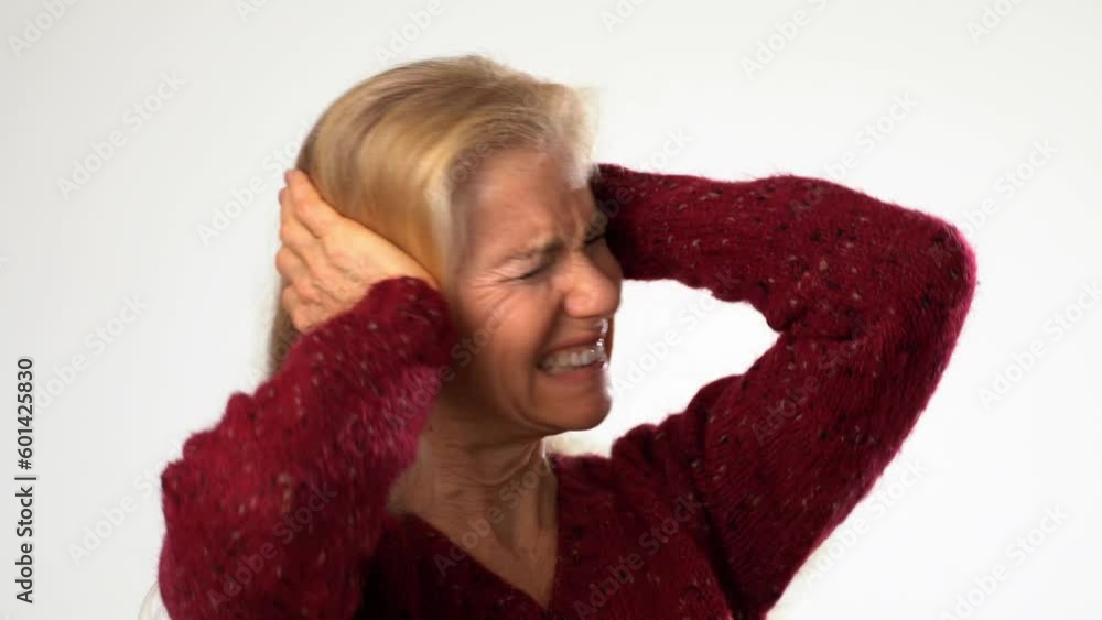 Closeup of unhappy displeased mature older woman covering her ears with her hands because of loud noise standing model isolated on white background in studio