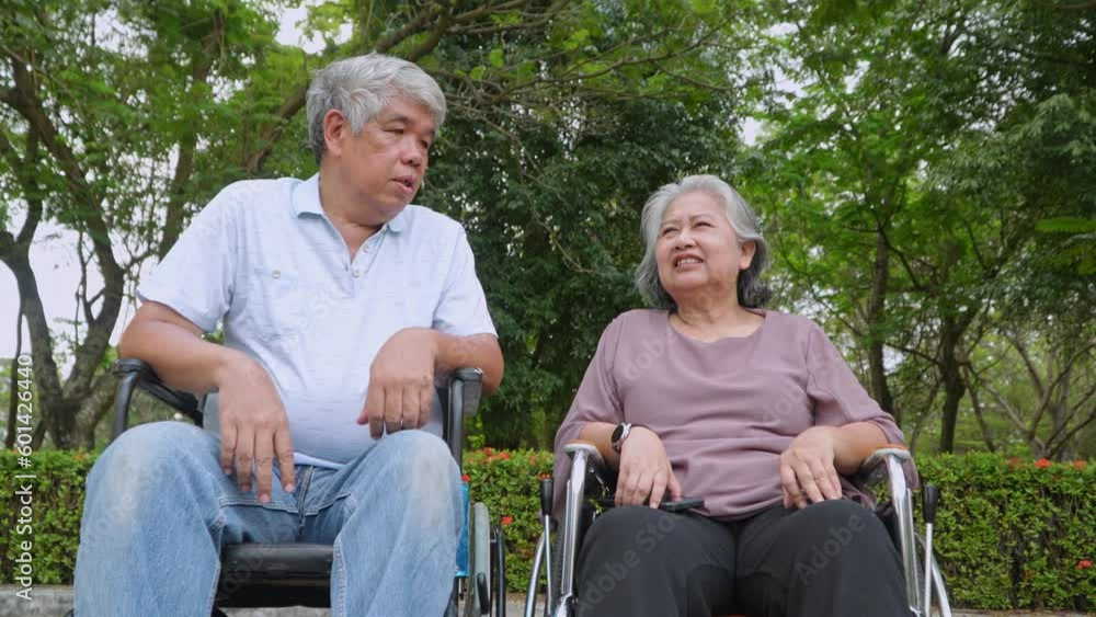 Happy Asian senior couple sitting in wheelchair and old woman holding husband hands and talking together and relaxing outdoors in the park, Leisure activities of retirees, elderly health care concept. Happy Asian senior couple sitting in wheelchair and old woman holding husband hands and talking together and relaxing outdoors in the park, Leisure activities of retirees, elderly health care concept.