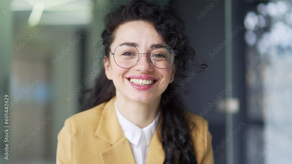 Portrait of a pretty smiling businesswoman in a suit and glasses sitting in a modern office looking at camera. Happy curly brunette posing with a cheerful look Headshot of a positive female manager Portrait of a pretty smiling businesswoman in a suit and glasses sitting in a modern office looking at camera. Happy curly brunette posing with a cheerful look Headshot of a positive female manager