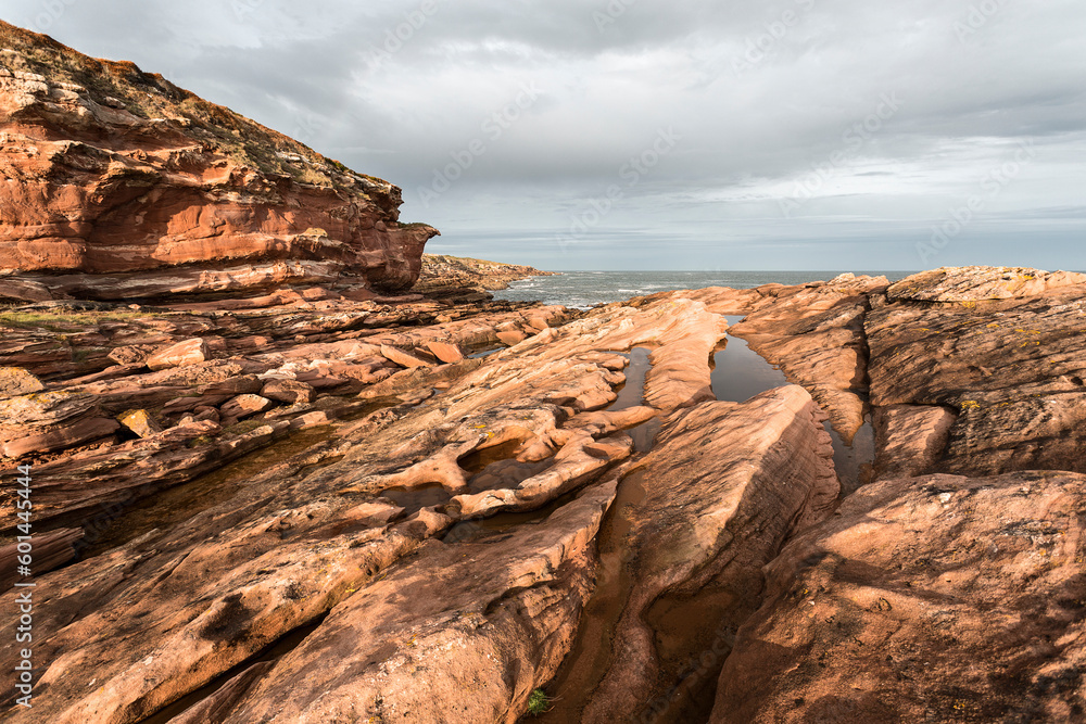Cliff and rocky area on the north coast of Scotland, sunset with reddish stones with cloudy sky.
