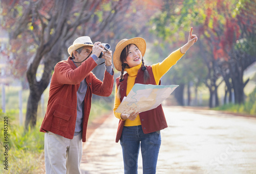 asian father and daughter spend time to travel together in autumn park,young female holding a map and pointing to something,senior man is taking a photo, concept of family,travel,the love of a family