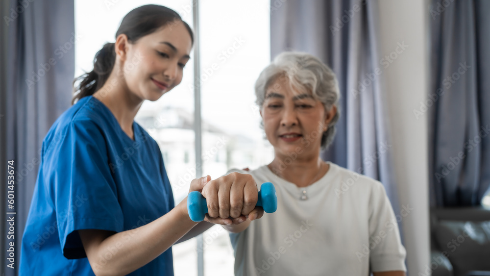 Obraz premium Young physiotherapist helping senior mature asian woman grey hair work out with dumbbells, to recover from injury at health centre in physical therapy session.