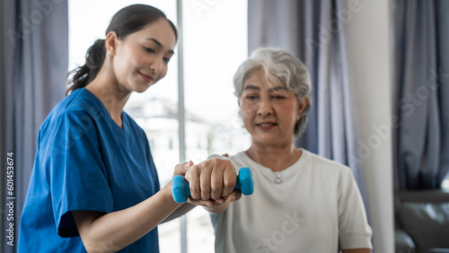 Young physiotherapist helping senior mature asian woman grey hair work out with dumbbells, to recover from injury at health centre in physical therapy session.