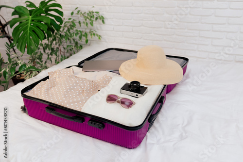Open travel suitcase with women's clothing on the bed