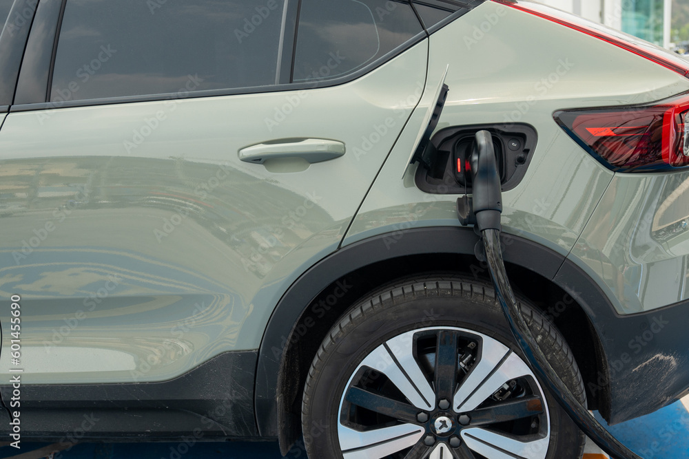 The side of the green metallic car with a power cable supply that nobody held, plugged into a car's charging port to charge pure electricity that parking in charging station. Copy space on the left. The side of the green metallic car with a power cable supply that nobody held, plugged into a car's charging port to charge pure electricity that parking in charging station. Copy space on the left.