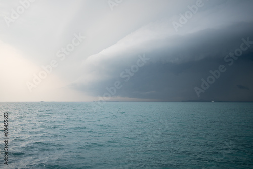 The view of crystal clear and calm turquoise seawater that sea surface move softly because of the wind, with an overcast big rain cloud that gradually moves to replace the clear sky in the background.