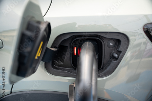 Close-up and selective focus of car's charging port with the red light that indicating the charging status with a blurred power cable supply plugged in, to charge pure electricity for electric vehicle