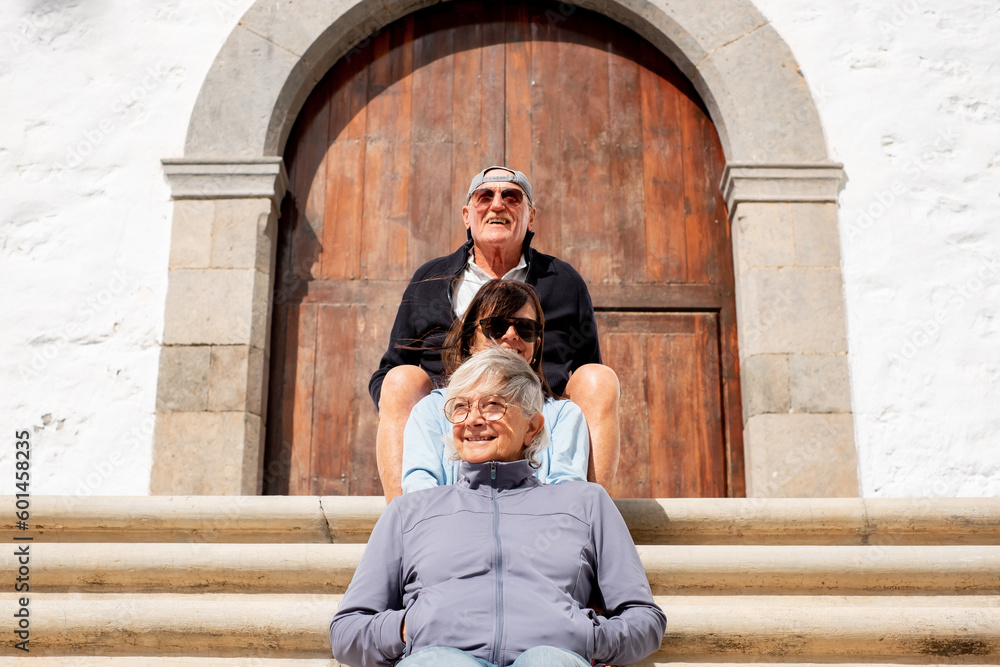 Group of senior friends sitting outdoors on the steps in front of an old wooden church door. Three retired women and a man smiling in sunny day