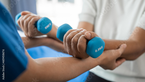 Fotografia Young physiotherapist helping senior mature asian woman grey hair work out with dumbbells, to recover from injury at health centre in physical therapy session