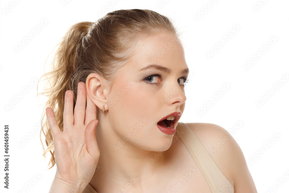 Fototapeta premium Young caucasian blonde woman listening to something by putting hand on the ear on a white background