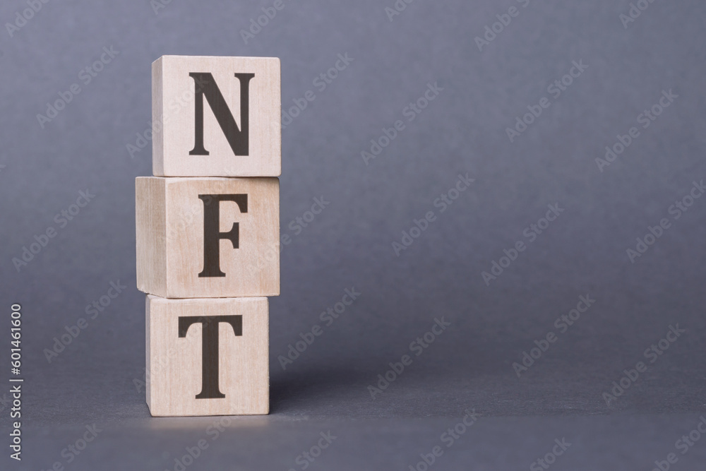 Concept word NFT on wooden cubes on a gray background. inscription on a financial, business or economic theme. NFT - short for Non Fungible Token Concept word NFT on wooden cubes on a gray background. inscription on a financial, business or economic theme. NFT - short for Non Fungible Token