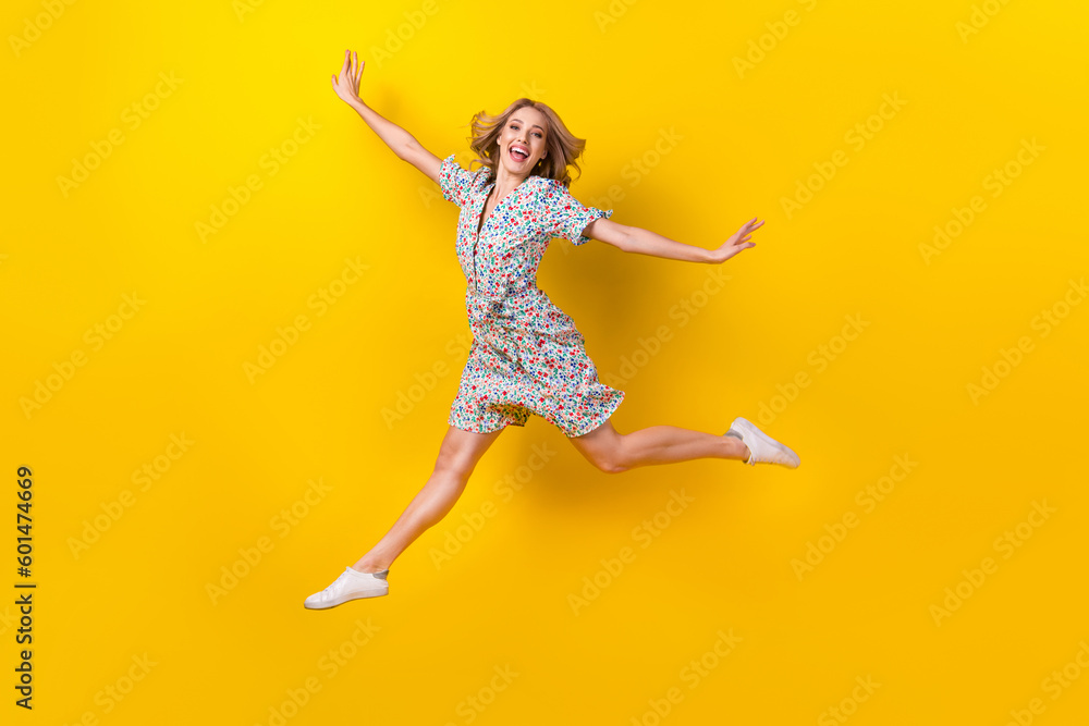 Full length photo of cute funky woman dressed flower print sarafan arms sides jumping high isolated yellow color background - obrazy, fototapety, plakaty 