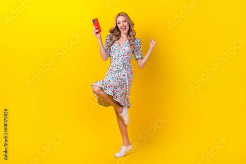 Full length photo of lucky cute woman dressed print sarafan winning game iphone samsung apple device isolated yellow color background