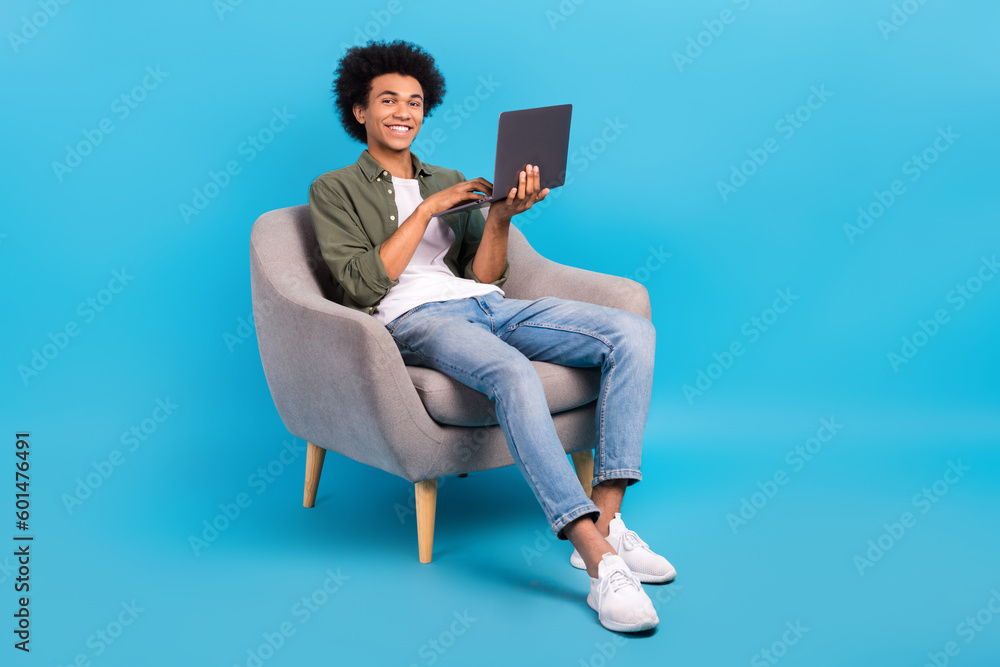 Full size portrait of handsome person sit chair use netbook eshopping isolated on blue color background Full size portrait of handsome person sit chair use netbook eshopping isolated on blue color background