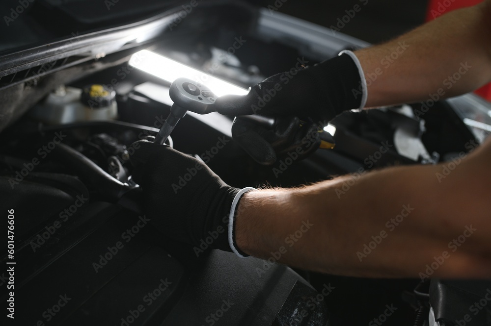 A mechanic is doing car checkup under the hood with flashlight at mechanic's shop.