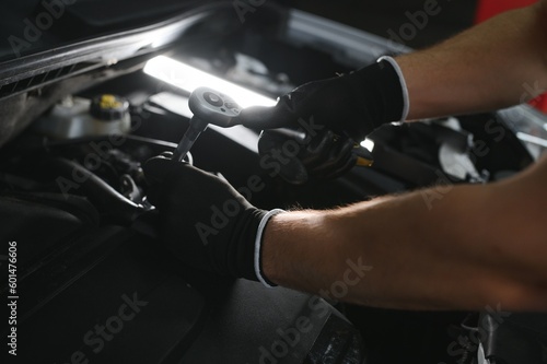A mechanic is doing car checkup under the hood with flashlight at mechanic's shop. © Serhii