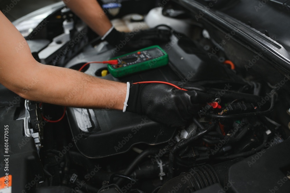 Fototapeta premium Car mechanic is using a multimeter with voltage range measurement to check the voltage level of the car battery.