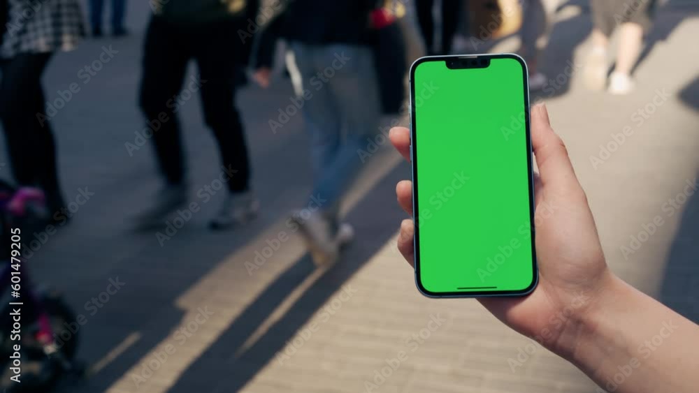Female Hand Holding Green Mock-up Screen Phone.Background Lively City Street Female Hand Holding Green Mock-up Screen Phone.Background Lively City Street
