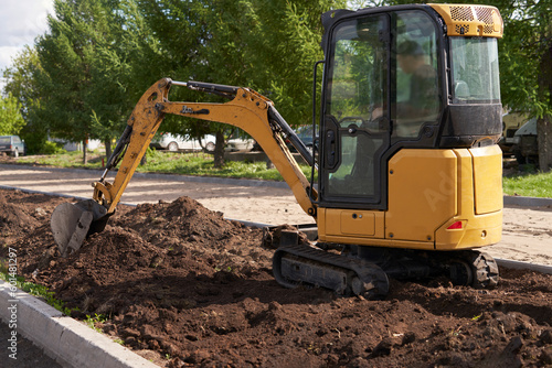 Mini excavator digs a ditch in the middle of the road in cramped urban conditions.