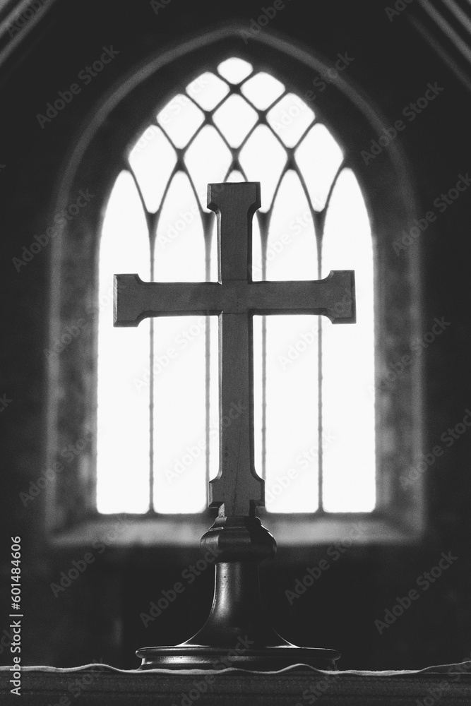 Serene black and white image of a cross in a church, framed by the delicate tracery of a window. Perfect for spiritual or religious projects.