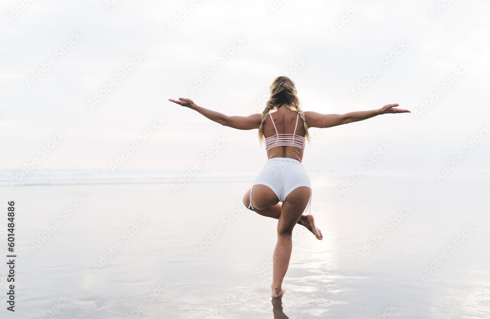 Back view of slim female yogi keeping healthy lifestyle and body wellbeing vitality, fit girl practice asana poses during sportive stretching at seashore beach - mindfulness enlightenment