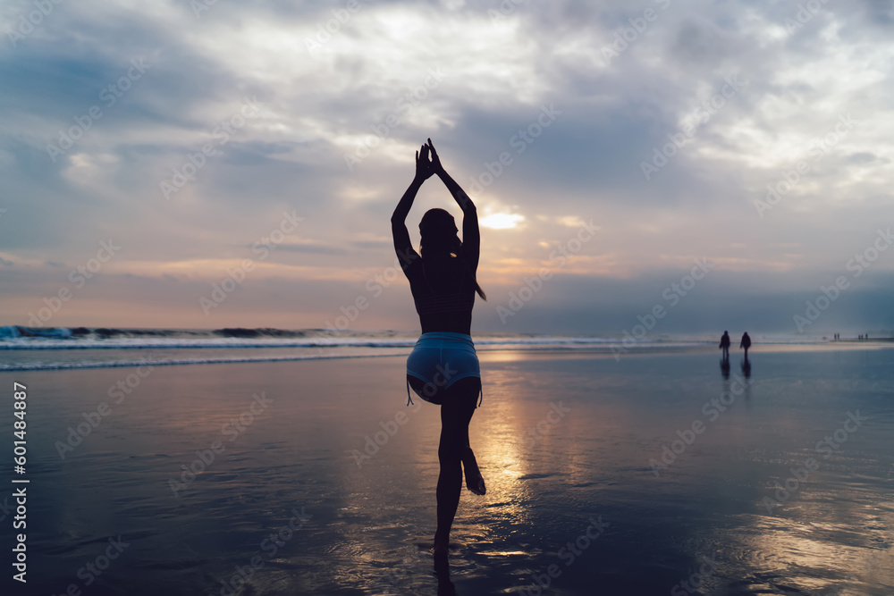 Back silhouette view of slim female yogi keeping healthy lifestyle and body wellbeing vitality, young fit girl in sportswear practice asana poses during sportive stretching at seashore beach