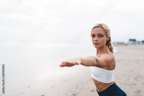 Caucasian female relaxing during morning yoga training at coastline beach feeling harmony and balance, calm fit girl enjoying hatha practice and yoga meditation for wellness during time at seashore
