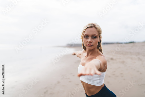 Portrait of calm blonde yogi looking at camera during pilates practice warm up at seashore beach, Caucasian female enjoying healthy lifestyle and weekend for sportive exercising for mindfulness © BullRun
