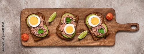 Wallpaper Mural Tuna toast. Open sandwich with tuna, rye bread, avocado and boiled egg on a wooden long board, brown grunge background. Top view, flat lay. Banner Torontodigital.ca