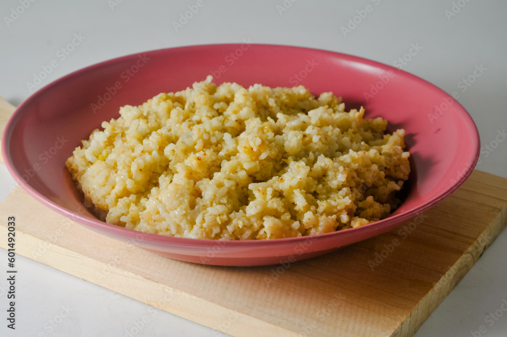 Fried rice, an Indonesian specialty, is served on a red plastic plate on a wooden board isolated on a white background