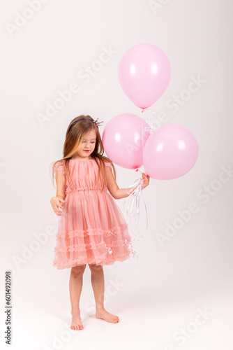 Cute smiling little girl in a pink princess dress posing with air balloons isolated on white background. Kids Birthday party celebration concept. Happy Birthday banner with copy space. Studio shot. © Irina Mikhailichenko