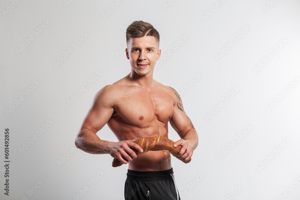 Happy handsome strong athlete fit guy with a hairstyle with a muscular body breaks a baguette bread on a white background. Healthy food and baking, concept Happy handsome strong athlete fit guy with a hairstyle with a muscular body breaks a baguette bread on a white background. Healthy food and baking, concept