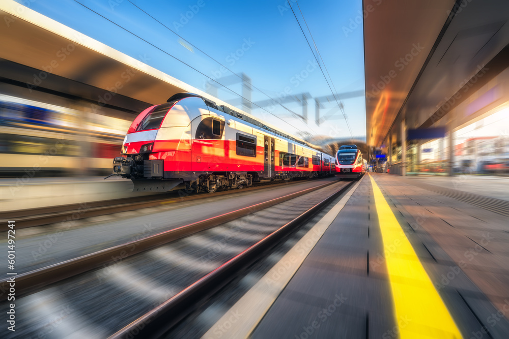 Orange high speed train in motion on the railway station at sunset. Fast moving modern intercity train and blurred background. Railway platform. Railroad in Austria. Passenger transportation. Concept