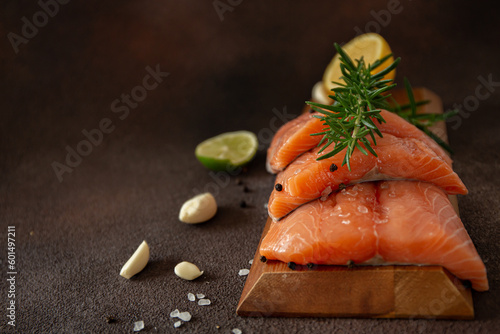 Slices of fresh salmon with herbs and lemon on wooden board on dark brown background