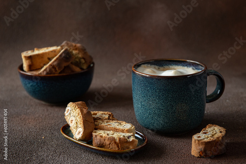 Billede på lærred Italian biscotti with hazelnuts with a blue cup of cappuccino on a dark brown ba