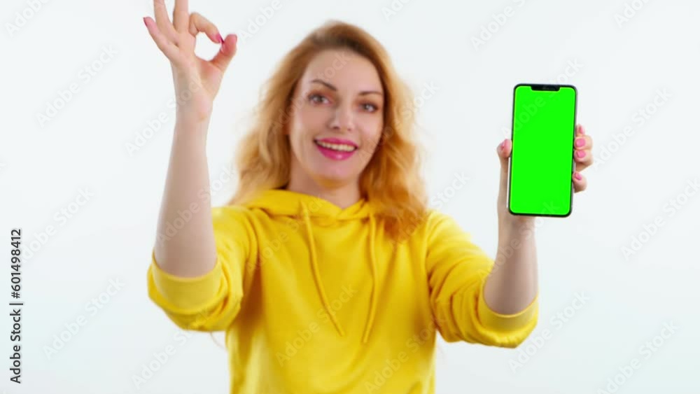 Green screen in camera focus, advertising, chroma key, OK gesture and woman with phone for product placement, branding and mobile app marketing. Smiling female with mobile smartphone, approval sign Green screen in camera focus, advertising, chroma key, OK gesture and woman with phone for product placement, branding and mobile app marketing. Smiling female with mobile smartphone, approval sign