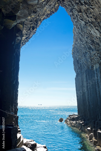 Fotografiet Iona island seen from the inside of the famous Fingal's Cave at Staffa island, dark basalt columns against blue summer sky, Inner Hebrides, Scotland