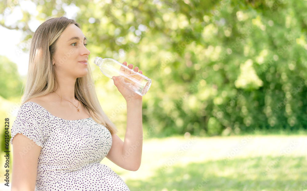 A pregnant woman is watching drinking water while sitting on a park bench. A pregnant woman is watching drinking water while sitting on a park bench.