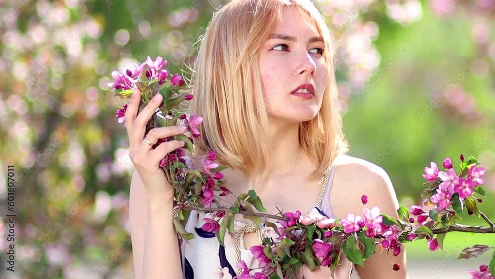 Portrait of a young woman posing holding a branch of a blossoming apple tree in her hand, against a bokeh background of pink flowers. Portrait of a young woman posing holding a branch of a blossoming apple tree in her hand, against a bokeh background of pink flowers.