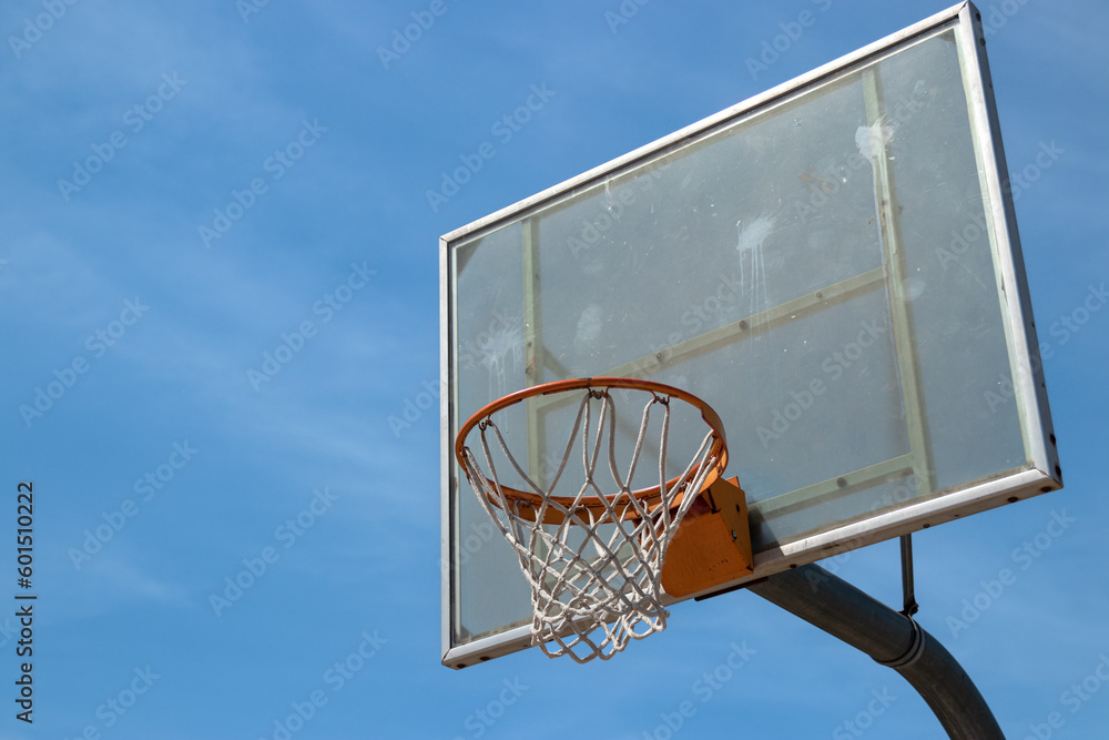 Naklejka premium Outdoor neighborhood basketball court park and recreational area, Basketball net and backboard against sunny blue sky with copy space