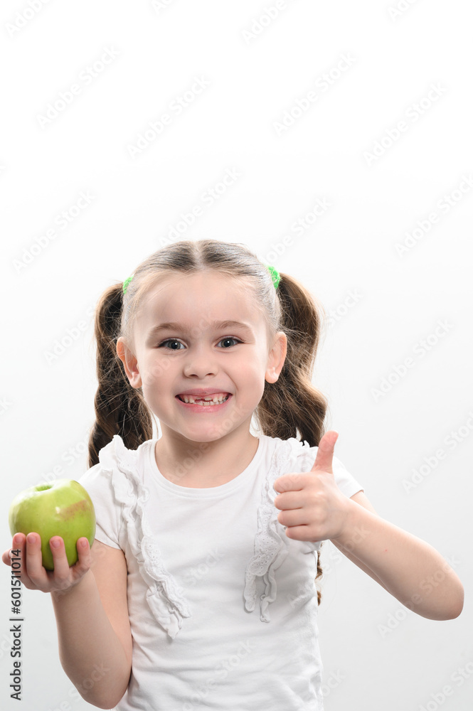 Portrait of a little girl holding a green apple in her hand and showing the class with her other hand Portrait of a little girl holding a green apple in her hand and showing the class with her other hand