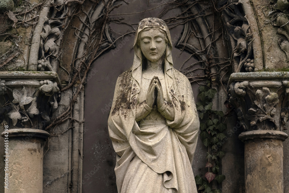 A old sculpture of  Virgin Mary. The stone statue is partially destroyed by time. Background in Gothic style