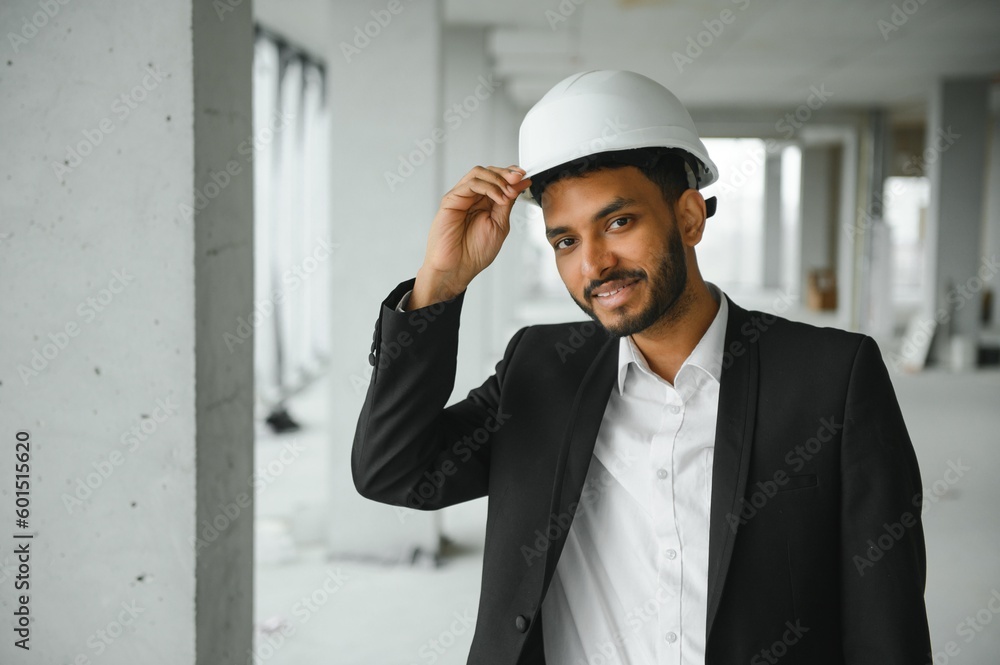 Indian construction site manager standing wearing helmet, thinking at construction site. Portrait of mixed race manual worker or architect. Indian construction site manager standing wearing helmet, thinking at construction site. Portrait of mixed race manual worker or architect.