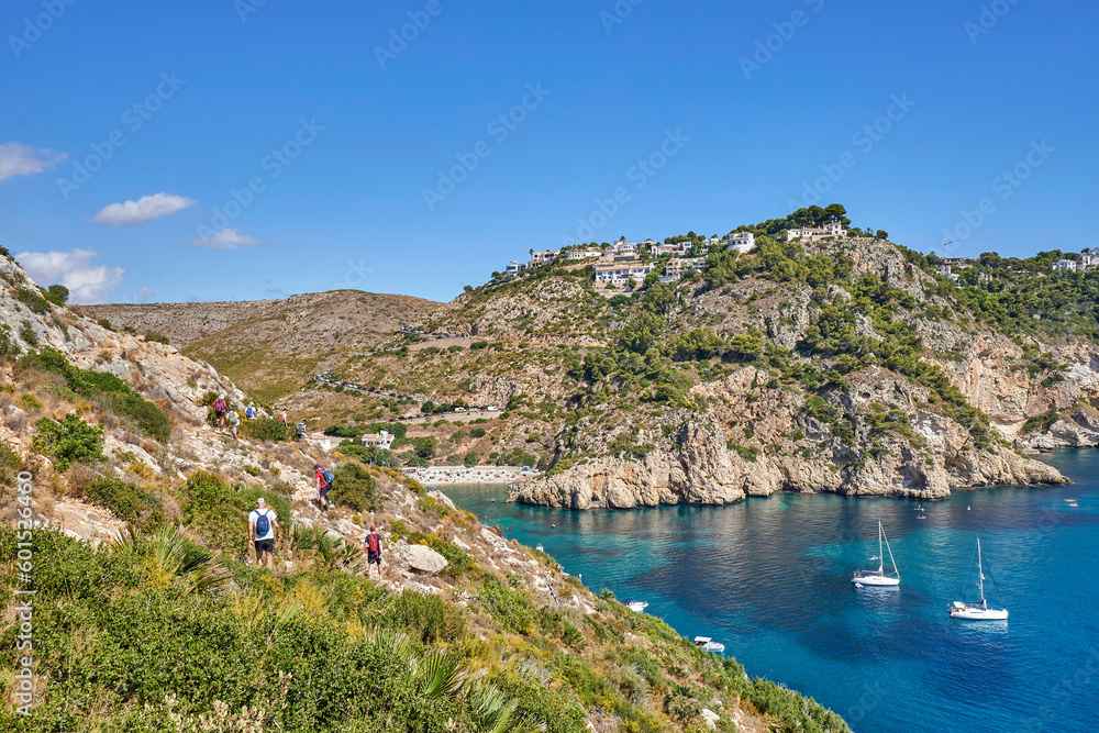 Hikers on the coast of Javea. In the background the famous La Granadella beach. Rustic cove with crystalline waters.In the Valencian Community, Alicante, Jávea, Spain.